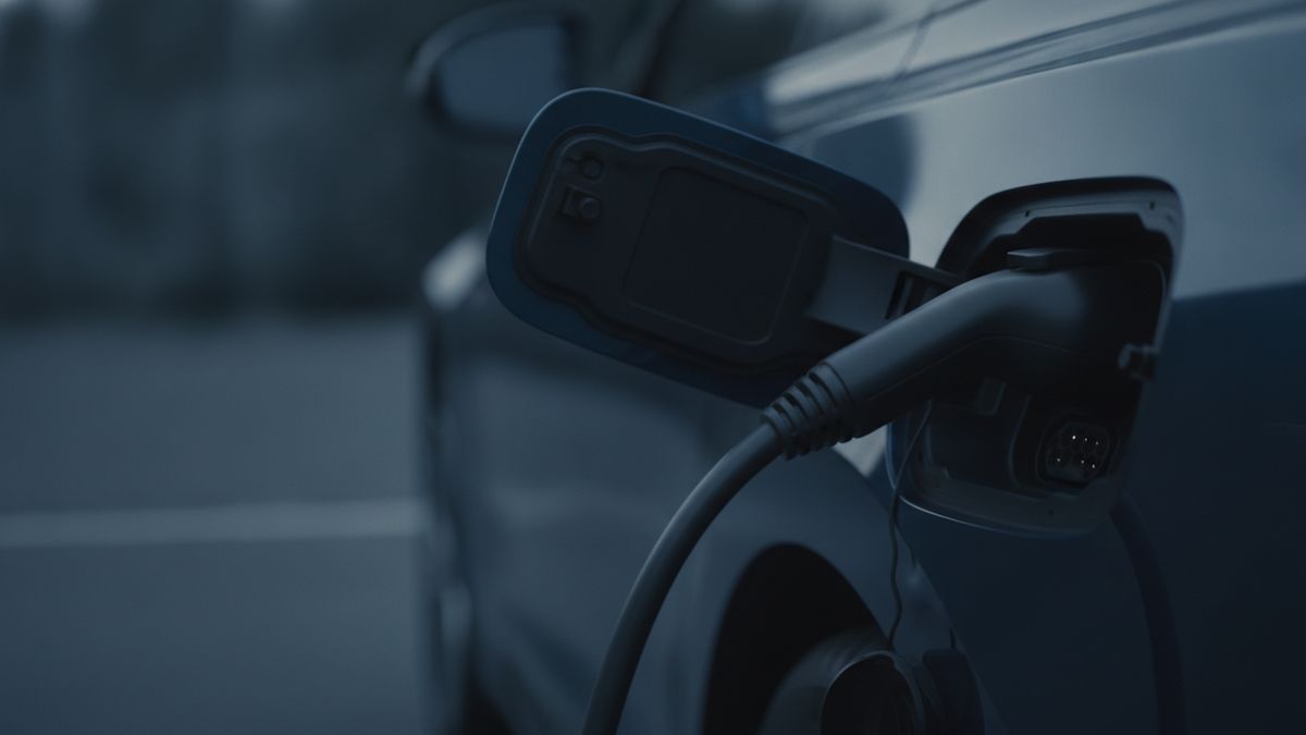A charging cable plugged into the open charge port of a modern electric car
